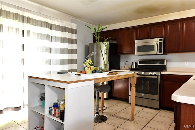 kitchen featuring a kitchen bar, stainless steel appliances, light countertops, and light tile patterned flooring