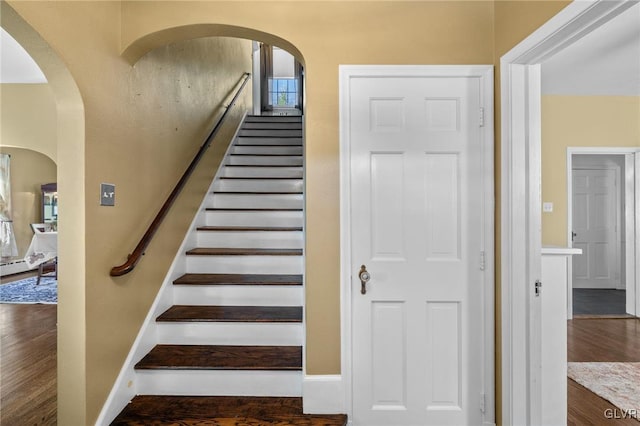 staircase with arched walkways, baseboards, and wood finished floors