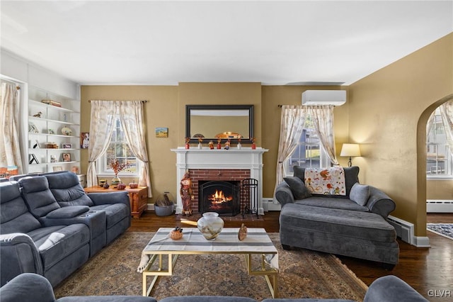 living area featuring a fireplace, a baseboard radiator, an AC wall unit, wood finished floors, and baseboards