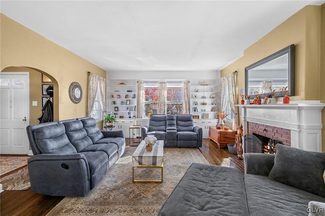 living room with a fireplace, built in features, arched walkways, and wood finished floors