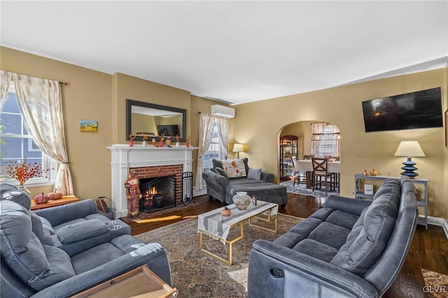 living area with arched walkways, dark wood-style flooring, and a brick fireplace