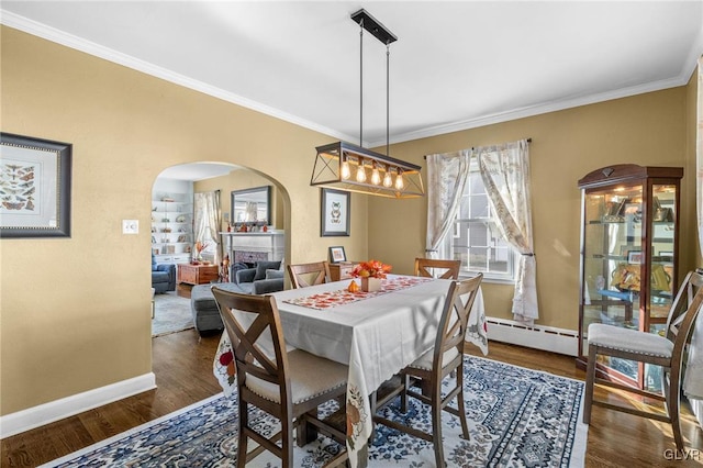 dining room with arched walkways, a baseboard radiator, wood finished floors, baseboards, and a tiled fireplace