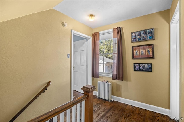 corridor featuring an upstairs landing, baseboards, dark wood finished floors, and radiator heating unit