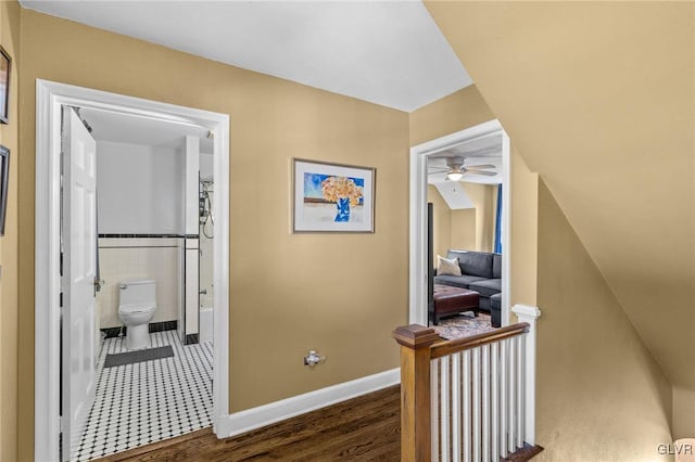 hallway featuring baseboards, tile walls, wood finished floors, and an upstairs landing