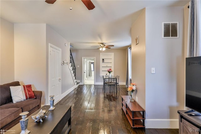 living area featuring ceiling fan, hardwood / wood-style flooring, visible vents, baseboards, and stairway