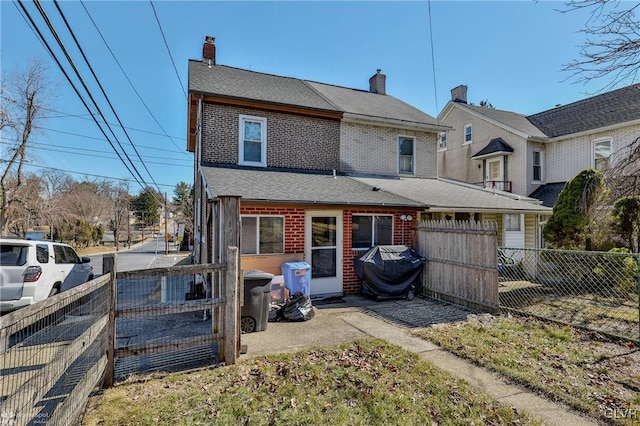 back of property with brick siding, a chimney, and fence