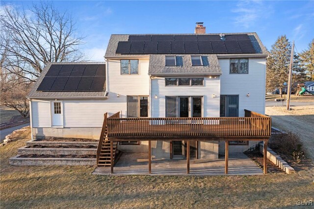 back of house with solar panels, a chimney, and a wooden deck