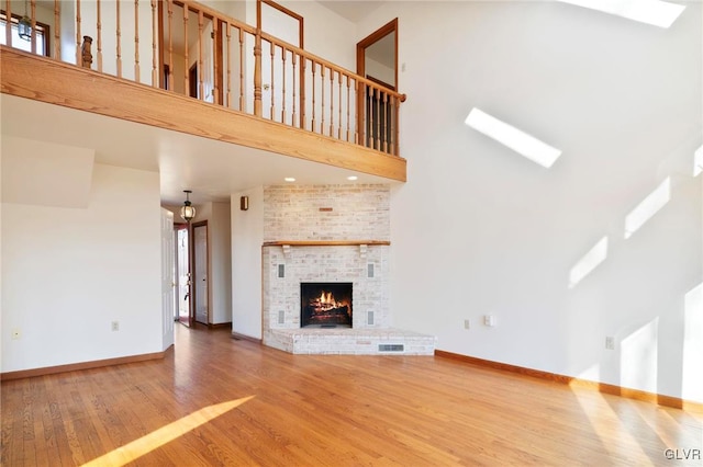 unfurnished living room with a high ceiling, a skylight, wood finished floors, and baseboards