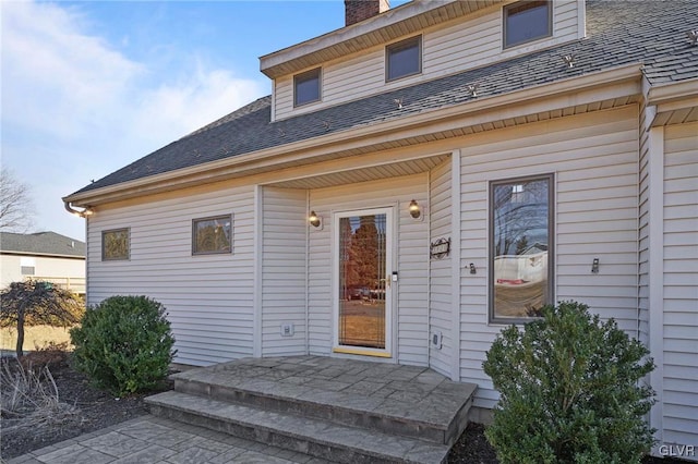 entrance to property with roof with shingles and a chimney