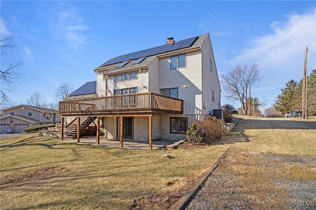 back of house with a deck, a patio, solar panels, a yard, and a chimney