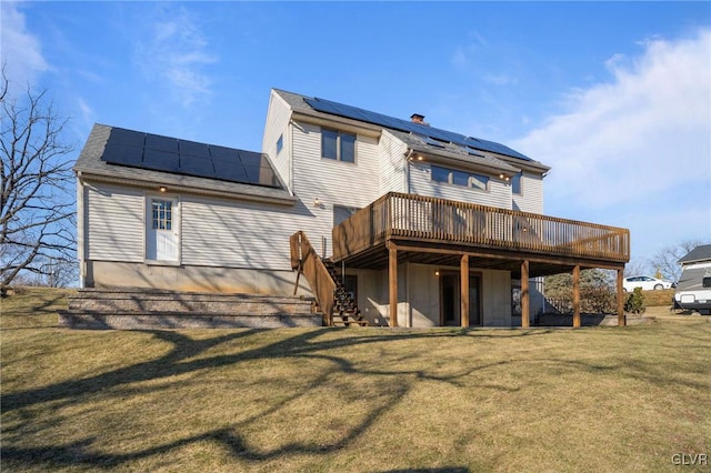 rear view of house with stairs, a yard, a wooden deck, and roof mounted solar panels