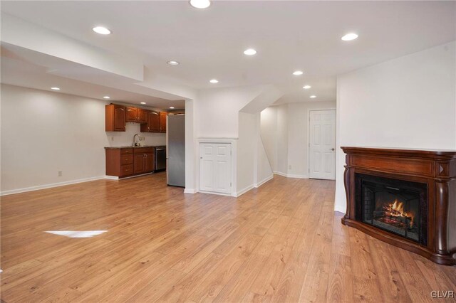 unfurnished living room featuring light wood finished floors, baseboards, a glass covered fireplace, a sink, and recessed lighting