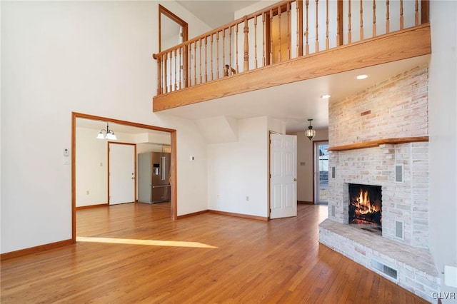 unfurnished living room featuring a fireplace, a towering ceiling, baseboards, and wood finished floors