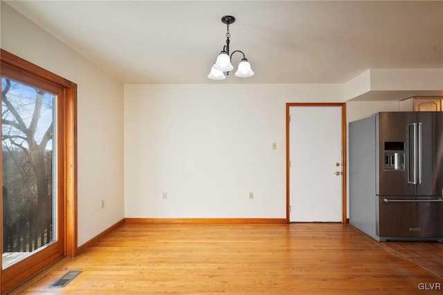 unfurnished dining area featuring light wood-type flooring, an inviting chandelier, baseboards, and visible vents