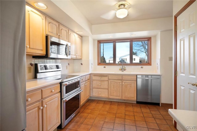 kitchen featuring light brown cabinets, stainless steel appliances, a sink, light countertops, and tasteful backsplash