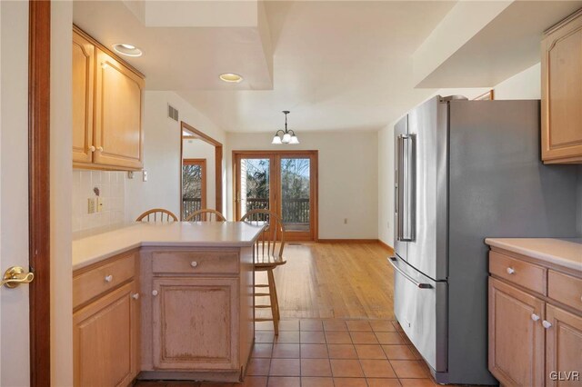 kitchen with light countertops, tasteful backsplash, a peninsula, and freestanding refrigerator