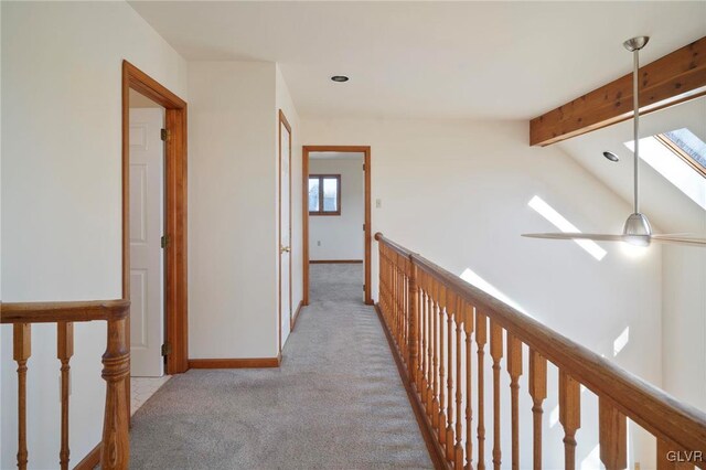 corridor featuring vaulted ceiling with skylight, baseboards, and light colored carpet