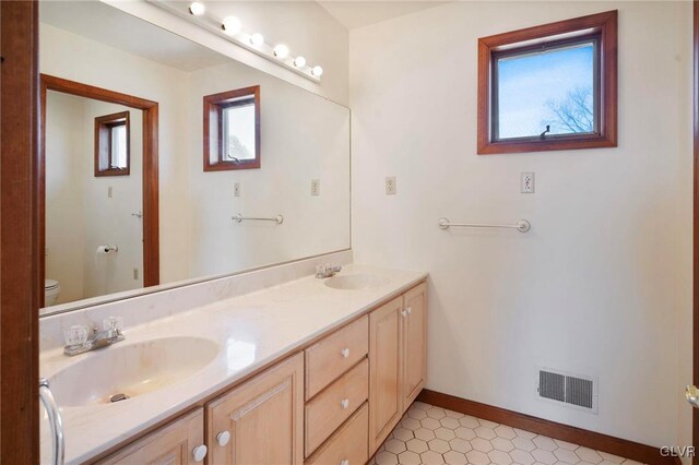 bathroom featuring toilet, double vanity, a sink, and visible vents