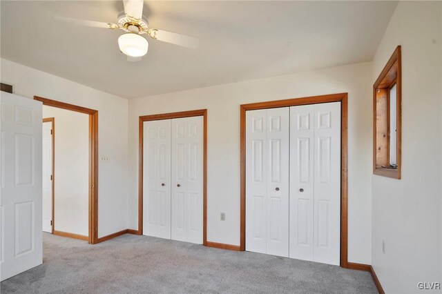 unfurnished bedroom featuring carpet flooring, ceiling fan, baseboards, and two closets