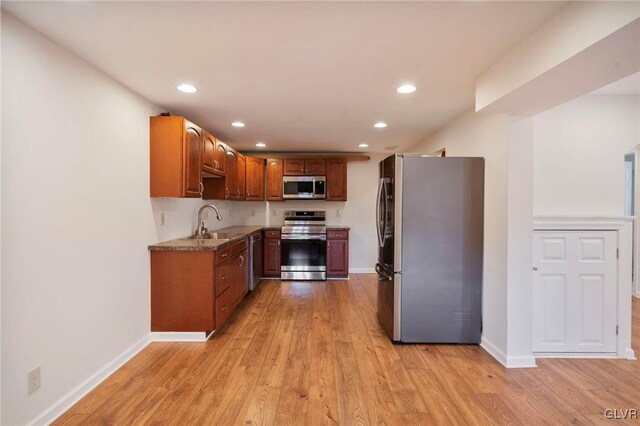 kitchen with stainless steel appliances, light wood-type flooring, a sink, and baseboards