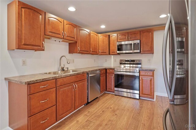 kitchen featuring light wood-style flooring, appliances with stainless steel finishes, brown cabinets, and a sink