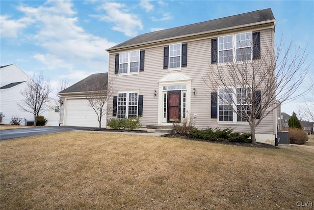 colonial-style house featuring an attached garage, aphalt driveway, central AC, and a front yard