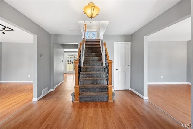 staircase with wood finished floors, visible vents, and baseboards