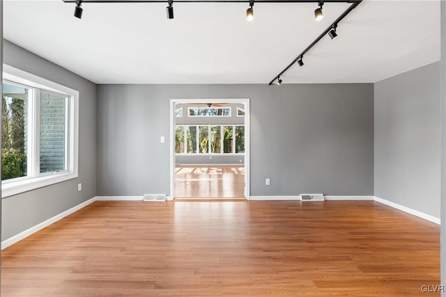 empty room with light wood finished floors, rail lighting, and visible vents