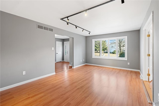 spare room with light wood-style flooring, track lighting, visible vents, and baseboards