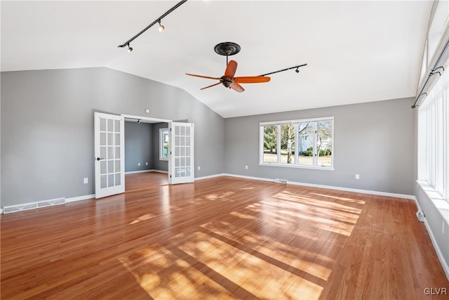 empty room featuring baseboards, ceiling fan, wood finished floors, vaulted ceiling, and french doors