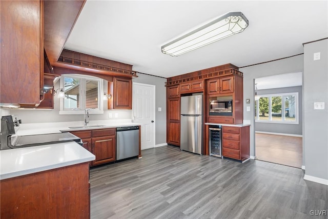 kitchen with beverage cooler, appliances with stainless steel finishes, light wood finished floors, and a sink