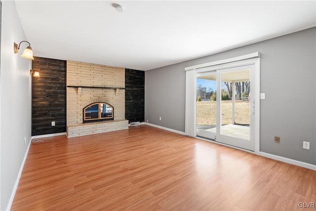 unfurnished living room with baseboards, wooden walls, a brick fireplace, and light wood-style floors