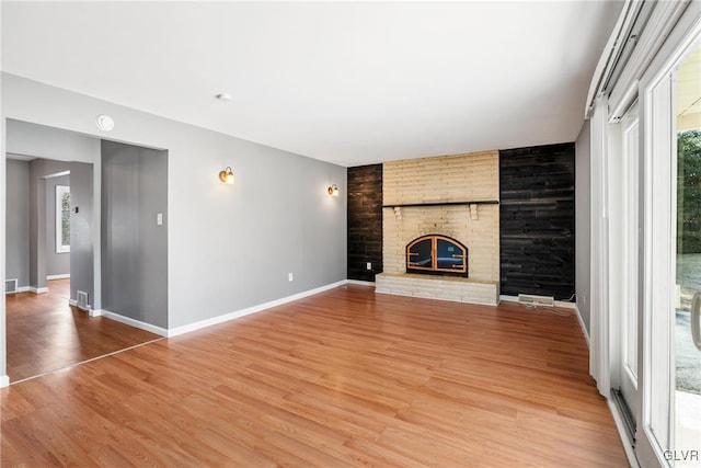 unfurnished living room with an accent wall, a fireplace, visible vents, baseboards, and light wood-style floors