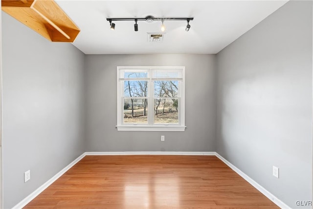 spare room featuring light wood finished floors, visible vents, and baseboards