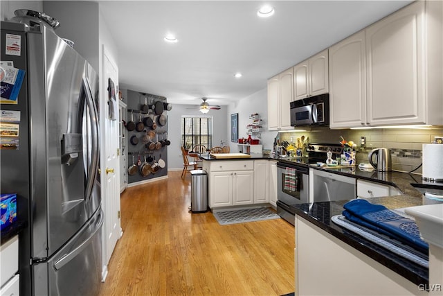 kitchen with backsplash, appliances with stainless steel finishes, light wood-style floors, a ceiling fan, and a peninsula