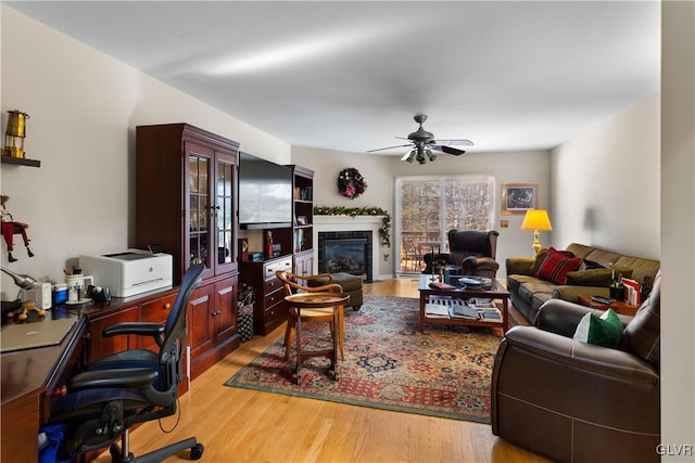 living area with ceiling fan, a glass covered fireplace, and light wood-style floors