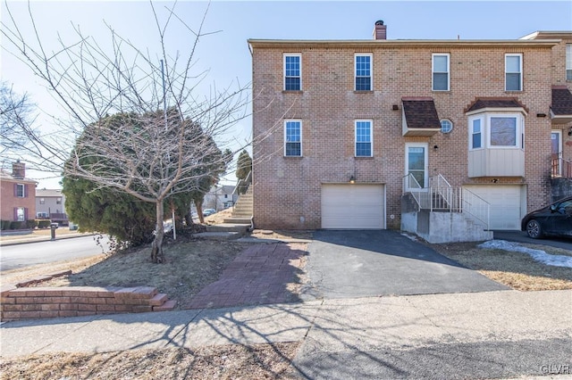 view of front of home with a garage, a chimney, aphalt driveway, and brick siding