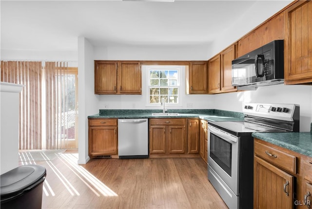 kitchen featuring appliances with stainless steel finishes, light wood-type flooring, brown cabinetry, and a sink