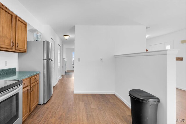 kitchen featuring dark countertops, brown cabinetry, stainless steel range with electric stovetop, light wood-type flooring, and baseboards