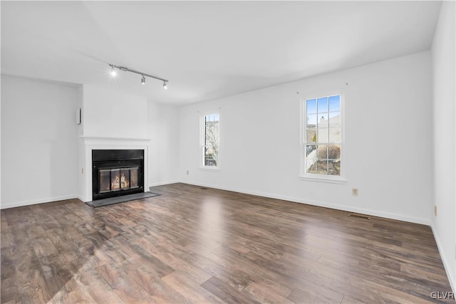 unfurnished living room with wood finished floors, a fireplace with flush hearth, a wealth of natural light, and baseboards