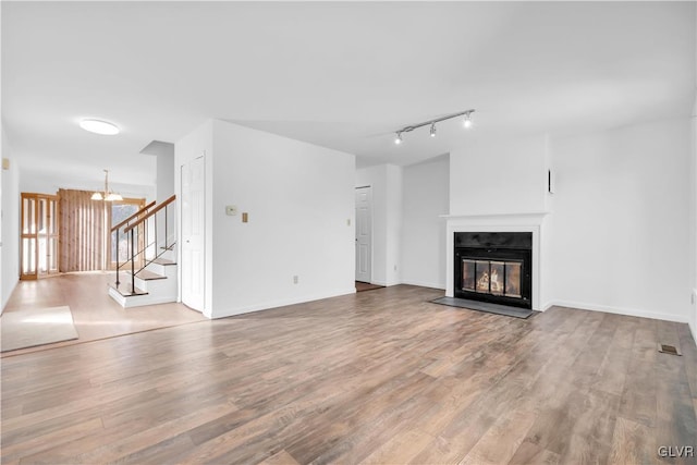 unfurnished living room with baseboards, a fireplace with flush hearth, wood finished floors, stairs, and a notable chandelier