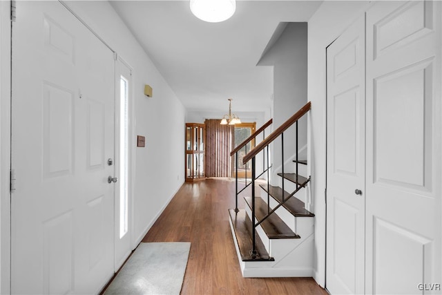 foyer entrance with wood finished floors, baseboards, an inviting chandelier, and stairs