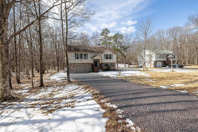 bi-level home featuring a garage, stone siding, and driveway