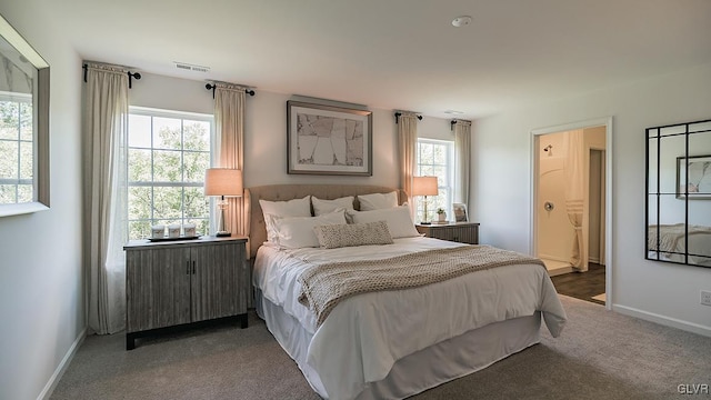 carpeted bedroom with ensuite bathroom, radiator heating unit, visible vents, and baseboards