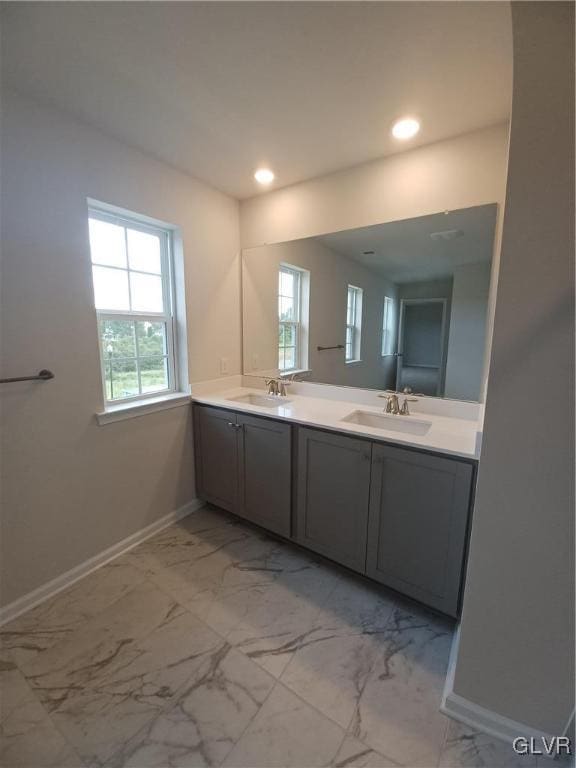 bathroom featuring double vanity, marble finish floor, baseboards, and a sink