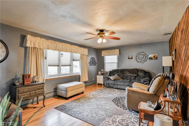 living room with light wood finished floors, a baseboard radiator, visible vents, and a ceiling fan