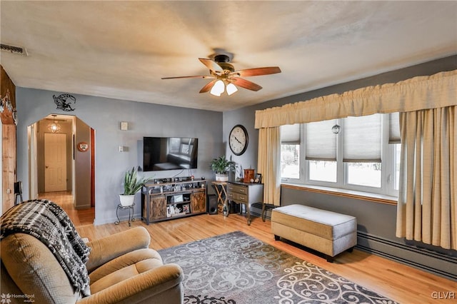 living area featuring arched walkways, a baseboard radiator, light wood-type flooring, and visible vents