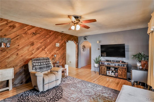 living area featuring a ceiling fan, arched walkways, wooden walls, and wood finished floors