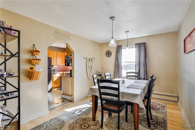 dining room with a baseboard radiator, arched walkways, light wood-style flooring, and baseboards