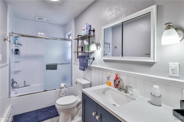 bathroom featuring bath / shower combo with glass door, wainscoting, vanity, and toilet